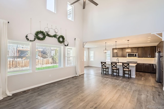 living room with ceiling fan, a high ceiling, baseboards, wood finished floors, and visible vents