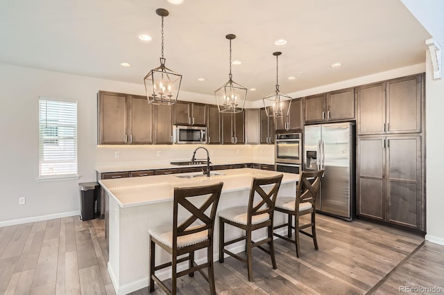 kitchen featuring a kitchen island with sink, light wood-style floors, light countertops, a chandelier, and stainless steel appliances