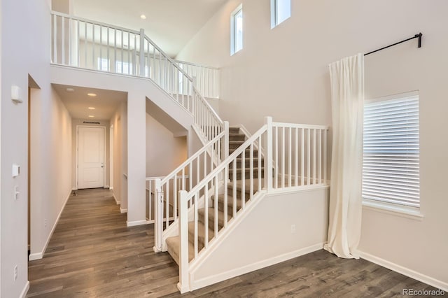 stairway featuring baseboards, wood finished floors, and a towering ceiling