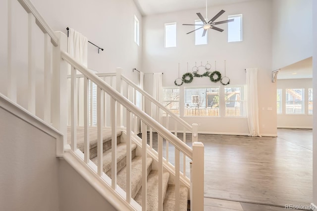 stairs featuring baseboards, a ceiling fan, a towering ceiling, and wood finished floors