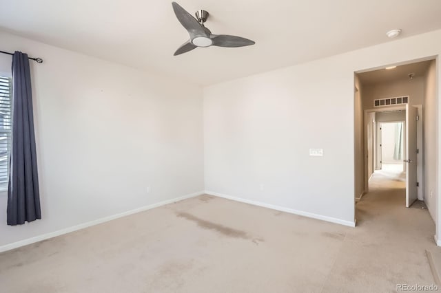 spare room with light colored carpet, a ceiling fan, baseboards, and visible vents