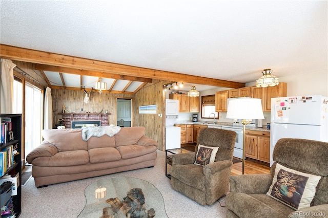 living room featuring sink, vaulted ceiling with beams, wooden walls, a fireplace, and light hardwood / wood-style floors