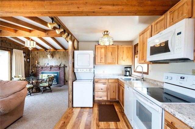 kitchen featuring sink, white appliances, stacked washer / drying machine, a fireplace, and wood walls