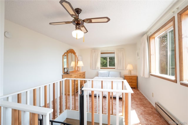 bedroom featuring a textured ceiling, carpet flooring, a nursery area, ceiling fan, and a baseboard heating unit