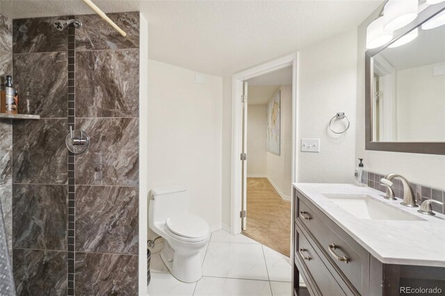 bathroom with a tile shower, vanity, toilet, a textured ceiling, and marble finish floor