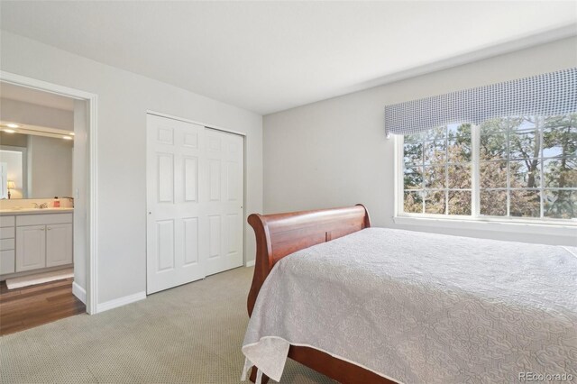 bedroom featuring connected bathroom, light carpet, a sink, baseboards, and a closet
