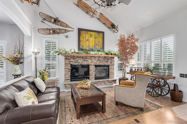 living room with ceiling fan, high vaulted ceiling, hardwood / wood-style flooring, and a stone fireplace