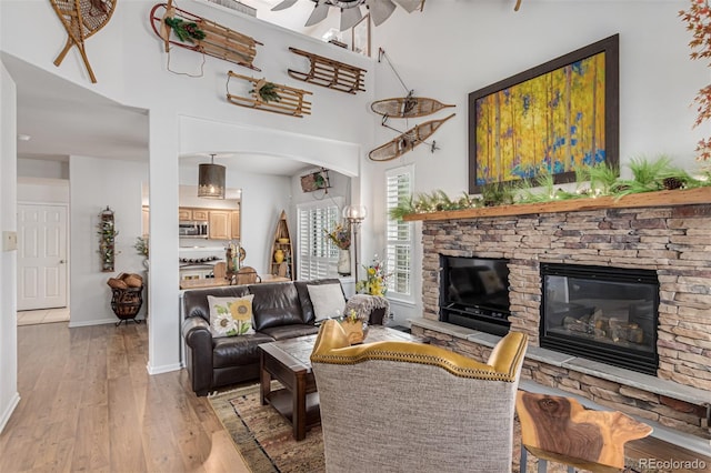 living room with ceiling fan, a stone fireplace, light hardwood / wood-style flooring, and a high ceiling