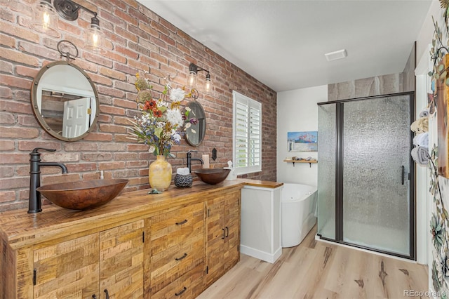 bathroom featuring wood-type flooring, vanity, plus walk in shower, and brick wall