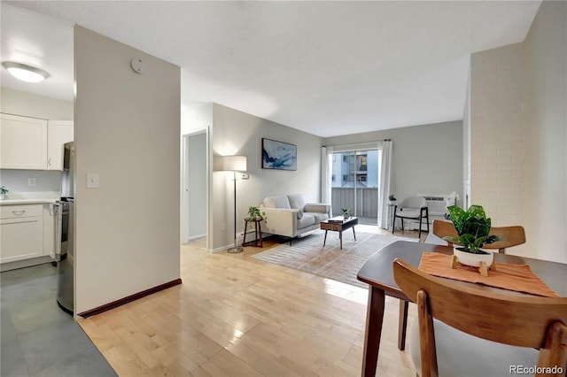 living area featuring light wood-style flooring, baseboards, and a wall mounted AC