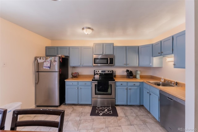 kitchen with sink, butcher block counters, blue cabinets, and appliances with stainless steel finishes