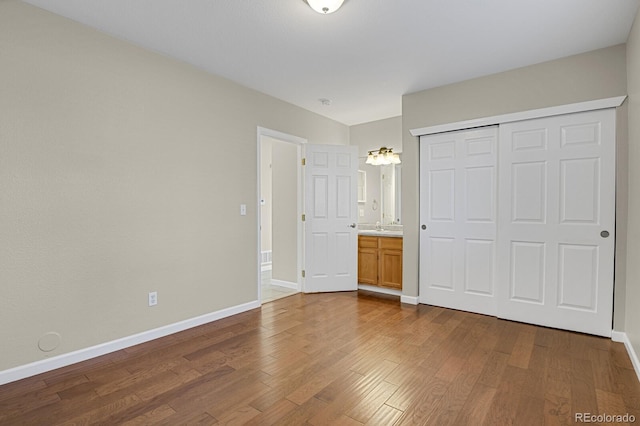 unfurnished bedroom with ensuite bathroom, a closet, sink, and hardwood / wood-style flooring