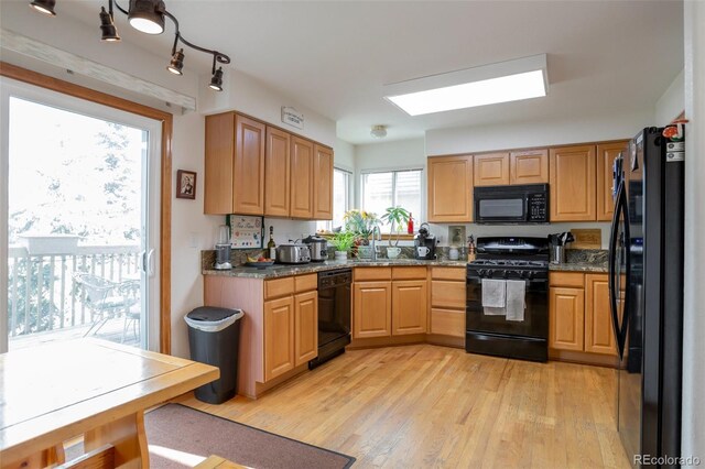 kitchen with light hardwood / wood-style floors, sink, black appliances, and dark stone countertops