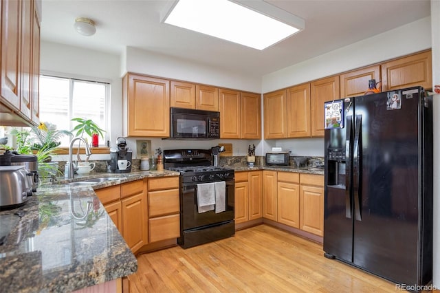 kitchen with black appliances, dark stone countertops, light hardwood / wood-style flooring, and sink