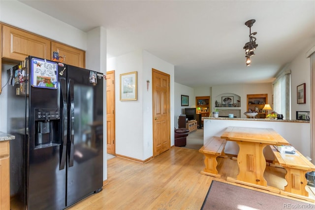 kitchen with light stone countertops, light wood-type flooring, decorative light fixtures, black fridge with ice dispenser, and light brown cabinets