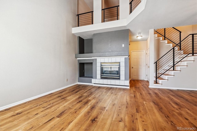 unfurnished living room with a tile fireplace, hardwood / wood-style floors, and a towering ceiling