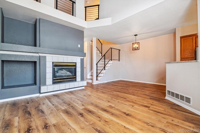 unfurnished living room with hardwood / wood-style floors, a high ceiling, and a tiled fireplace