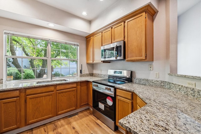 kitchen with light stone countertops, sink, light wood-type flooring, and appliances with stainless steel finishes