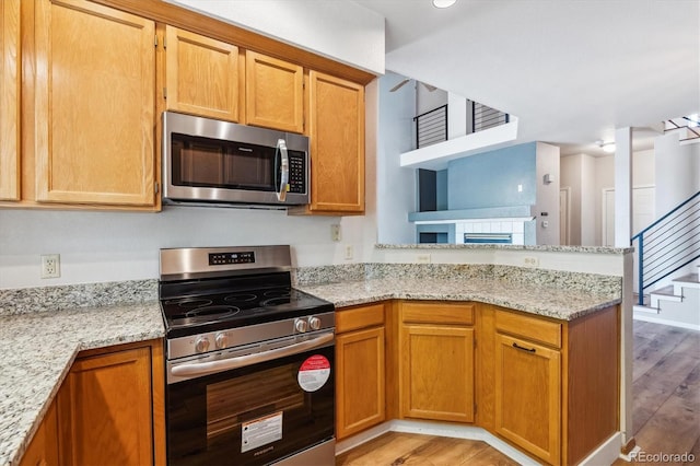 kitchen featuring light stone countertops, kitchen peninsula, stainless steel appliances, and light hardwood / wood-style flooring