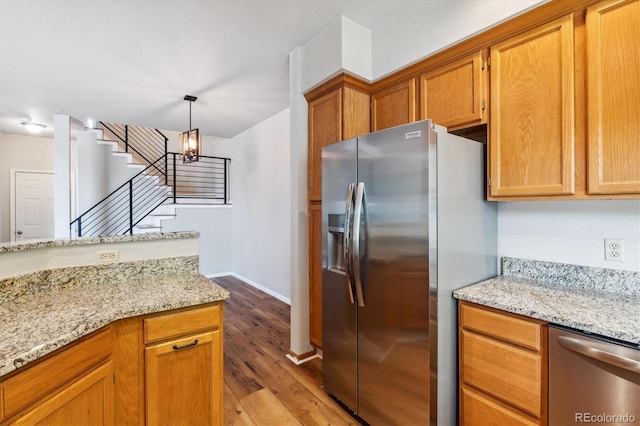 kitchen with light stone counters, stainless steel appliances, a notable chandelier, light hardwood / wood-style floors, and hanging light fixtures