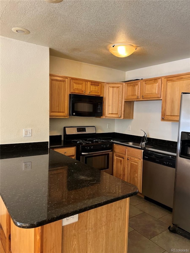 kitchen with appliances with stainless steel finishes, dark stone counters, tile floors, a textured ceiling, and sink