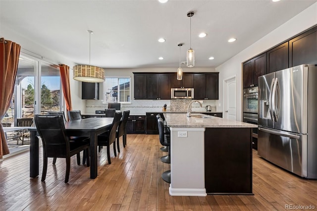 kitchen with tasteful backsplash, appliances with stainless steel finishes, a sink, dark brown cabinets, and light wood-type flooring