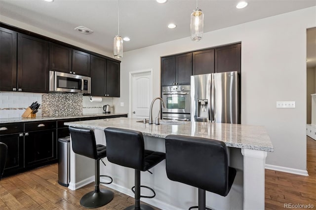 kitchen featuring tasteful backsplash, light stone counters, wood finished floors, stainless steel appliances, and a sink