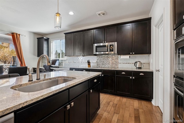 kitchen featuring hanging light fixtures, tasteful backsplash, stainless steel microwave, and a sink