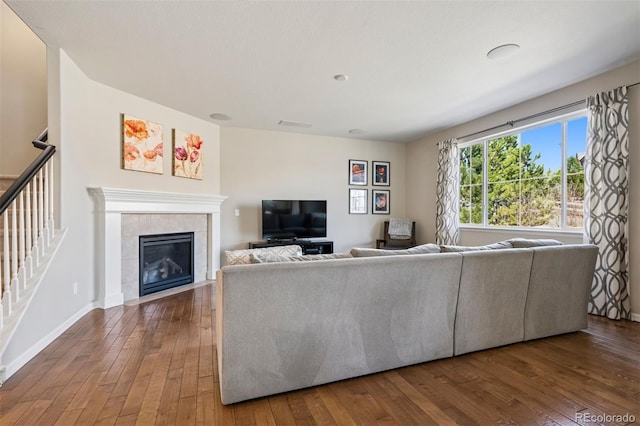 unfurnished living room featuring stairs, hardwood / wood-style floors, a tiled fireplace, and baseboards