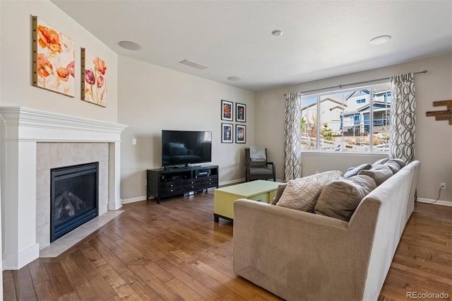 living area with a tile fireplace, visible vents, baseboards, and hardwood / wood-style flooring