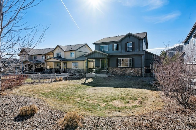 view of front of home featuring stone siding, fence, a front lawn, and board and batten siding