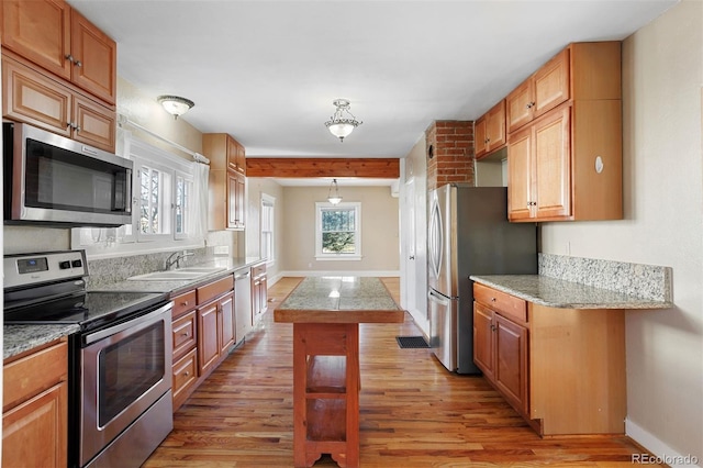 kitchen with sink, hanging light fixtures, stainless steel appliances, a kitchen island, and light wood-type flooring