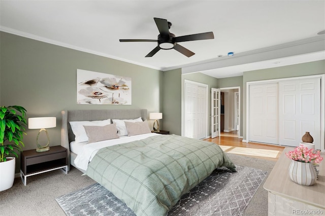 bedroom with carpet flooring, ceiling fan, crown molding, and two closets