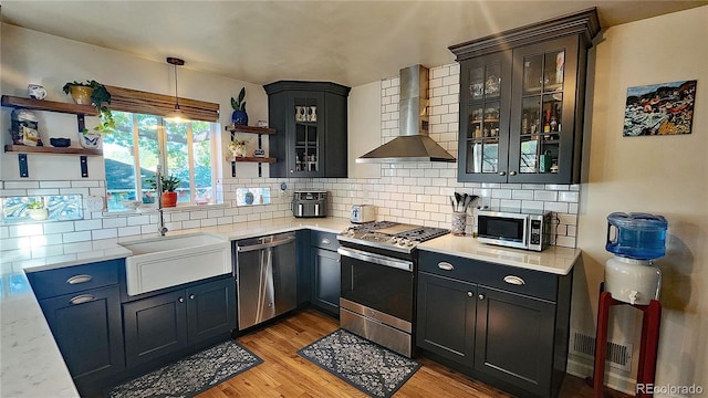 kitchen featuring light hardwood / wood-style floors, stainless steel appliances, hanging light fixtures, wall chimney exhaust hood, and sink