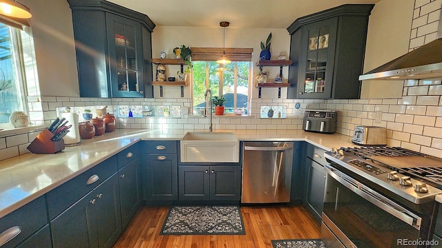 kitchen with stainless steel appliances, tasteful backsplash, hanging light fixtures, wall chimney exhaust hood, and sink