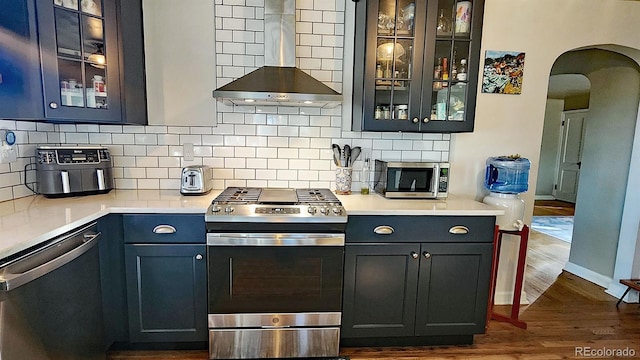 kitchen featuring dark wood-type flooring, stainless steel appliances, backsplash, and wall chimney range hood