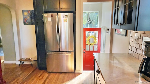 kitchen featuring pendant lighting, light hardwood / wood-style floors, backsplash, and stainless steel refrigerator