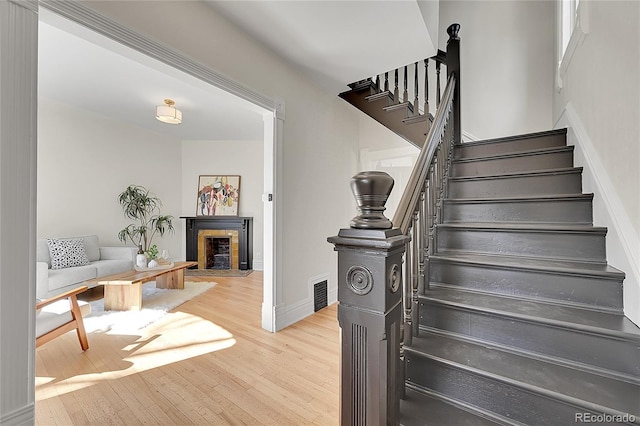 staircase featuring a fireplace with flush hearth, wood finished floors, visible vents, and baseboards