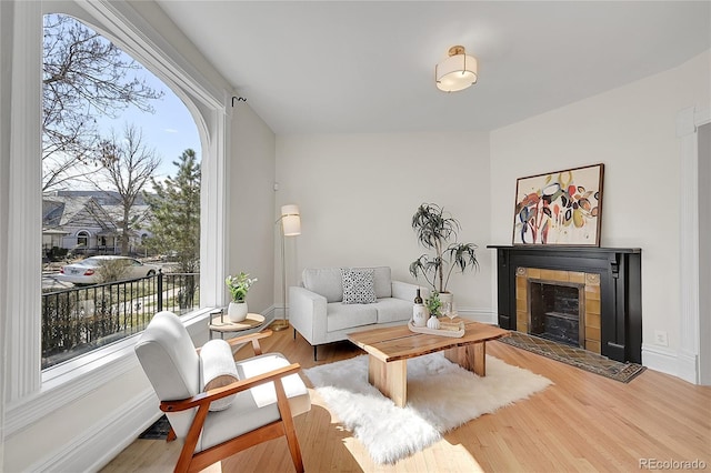 living area featuring plenty of natural light, wood finished floors, baseboards, and a tile fireplace