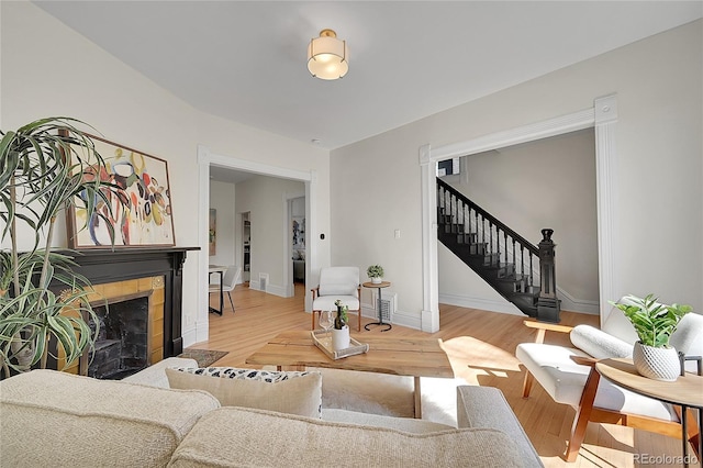 living area with stairway, a tile fireplace, baseboards, and wood finished floors