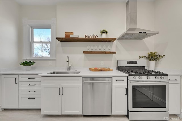 kitchen with a sink, wall chimney range hood, white cabinetry, appliances with stainless steel finishes, and light countertops