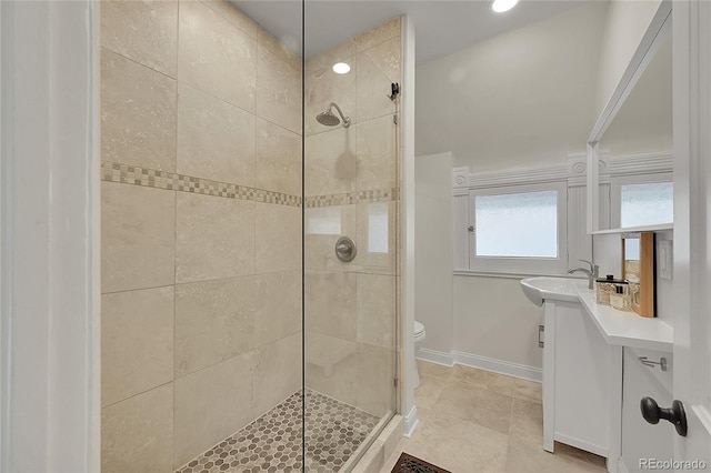 bathroom with a tile shower, toilet, vanity, and baseboards