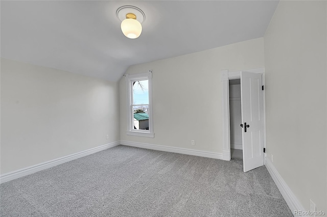 spare room featuring vaulted ceiling, carpet flooring, and baseboards