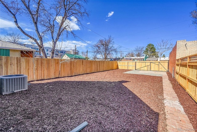 view of yard with central AC unit, a fenced backyard, and a gate