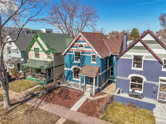 victorian home featuring stucco siding, roof with shingles, a porch, and a chimney