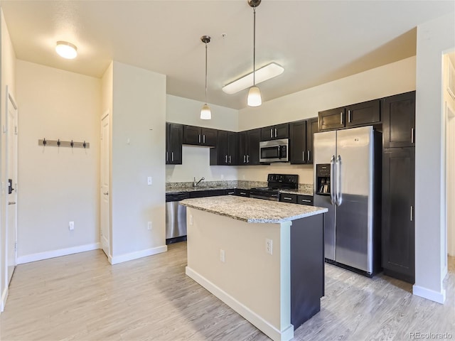 kitchen featuring appliances with stainless steel finishes, pendant lighting, sink, a center island, and light stone countertops