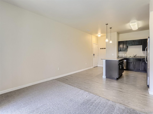 kitchen with sink, light stone counters, decorative light fixtures, a center island, and hardwood / wood-style floors