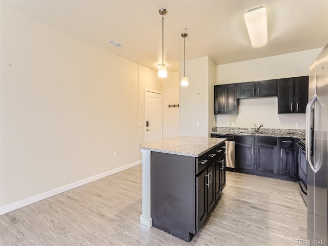 kitchen featuring decorative light fixtures, light hardwood / wood-style flooring, stainless steel appliances, and a kitchen island