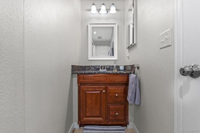 bathroom featuring a textured wall, vanity, and baseboards