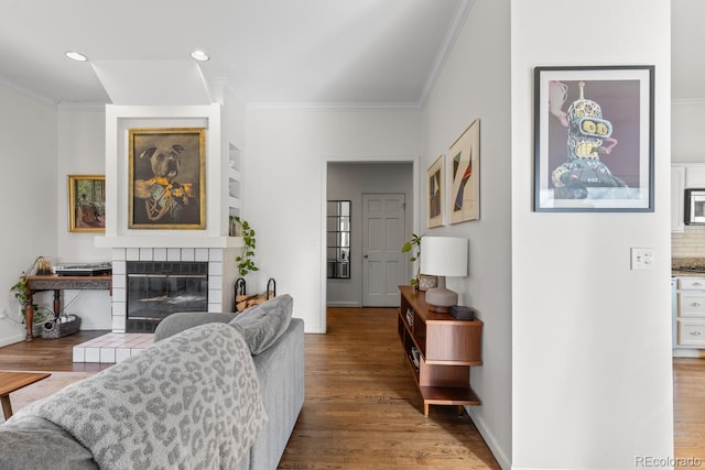 living area with recessed lighting, wood finished floors, baseboards, a tiled fireplace, and crown molding